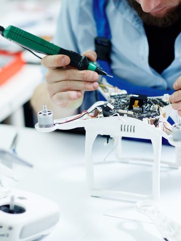 Closeup shot of unrecognizable man  testing electric current in circuit board of disassembled drone using multimeter tool on table in maintenance shop